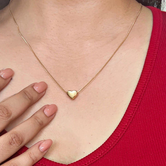 Gold heart-shaped necklace worn by a person in a red top.
